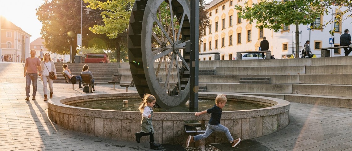 Zwei kleine Kinder rennen um das Wasserrad in Kempten